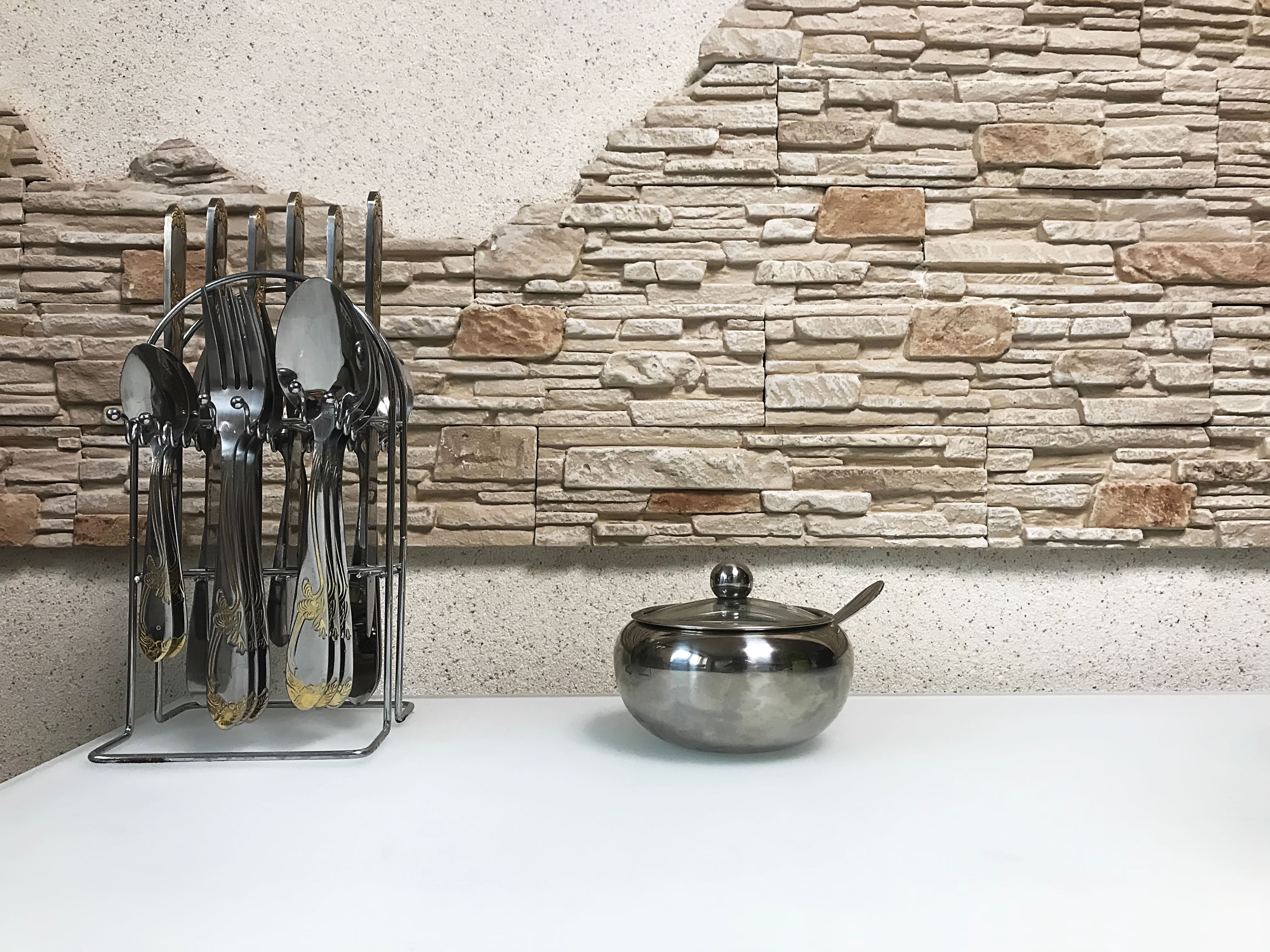 detalle de mesa de cocina con cubiertos y una pared de piedra artificial al fondo