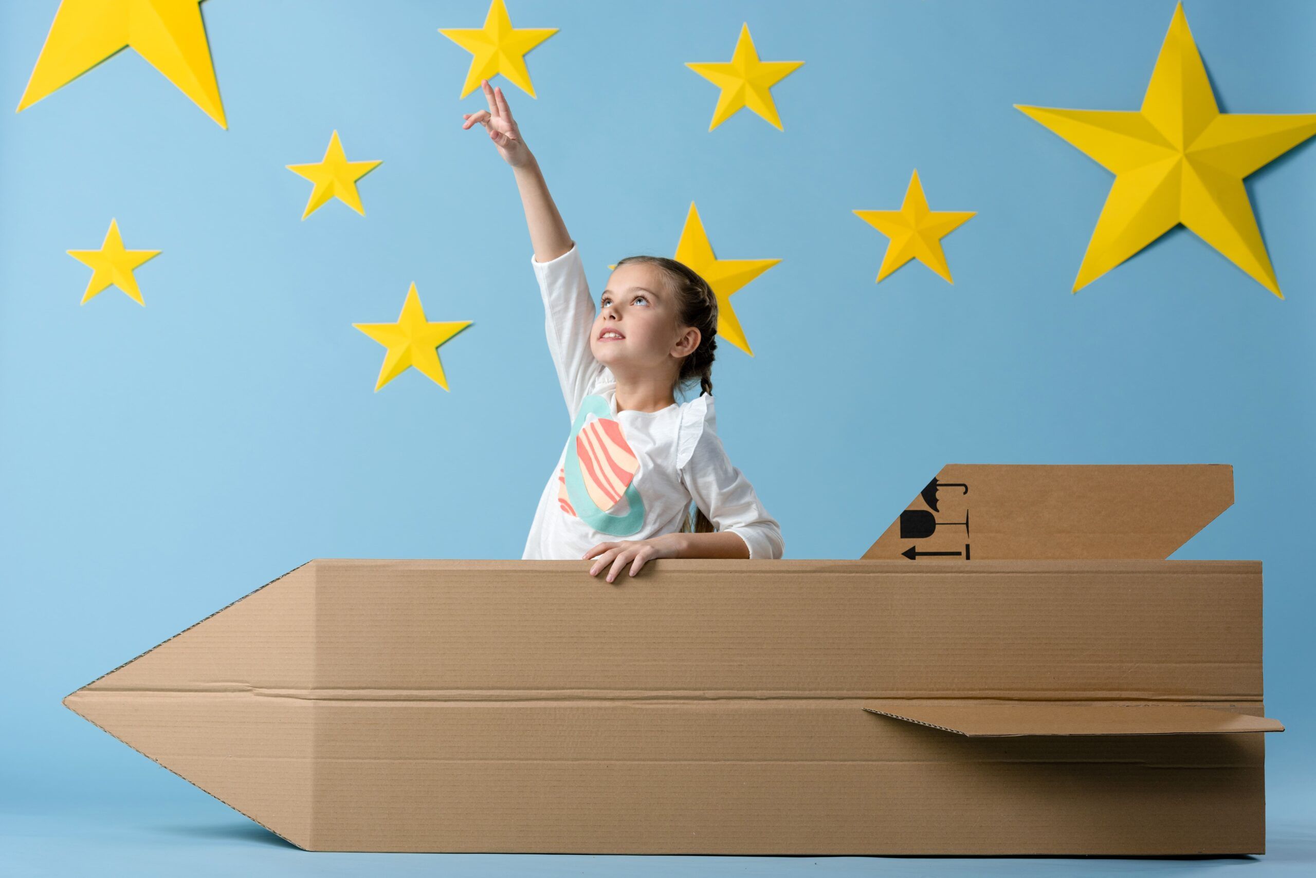 niña en un cohete de juguete apuntando hacia las estrellas